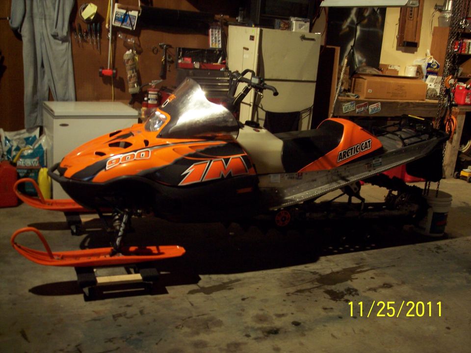 Orange and black Arctic Cat snowmobile with "900" visible on the front, parked indoors.