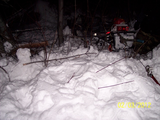 Snowmobile partially buried in snow at night, with a red gas can on the back.