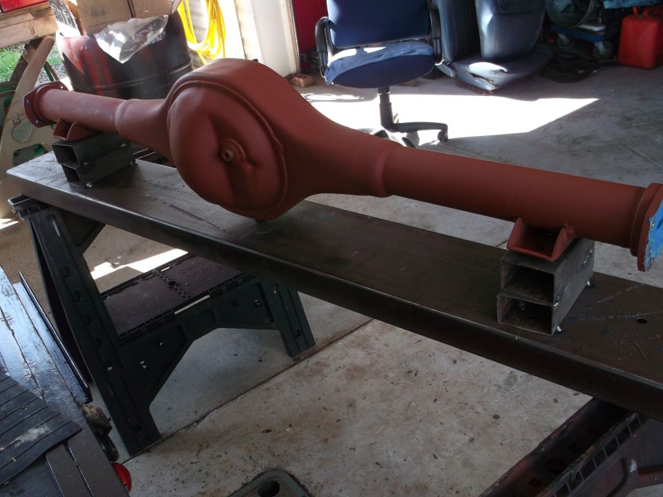 Red-primed Ford 9-inch rear axle assembly on sawhorses and workbench.
