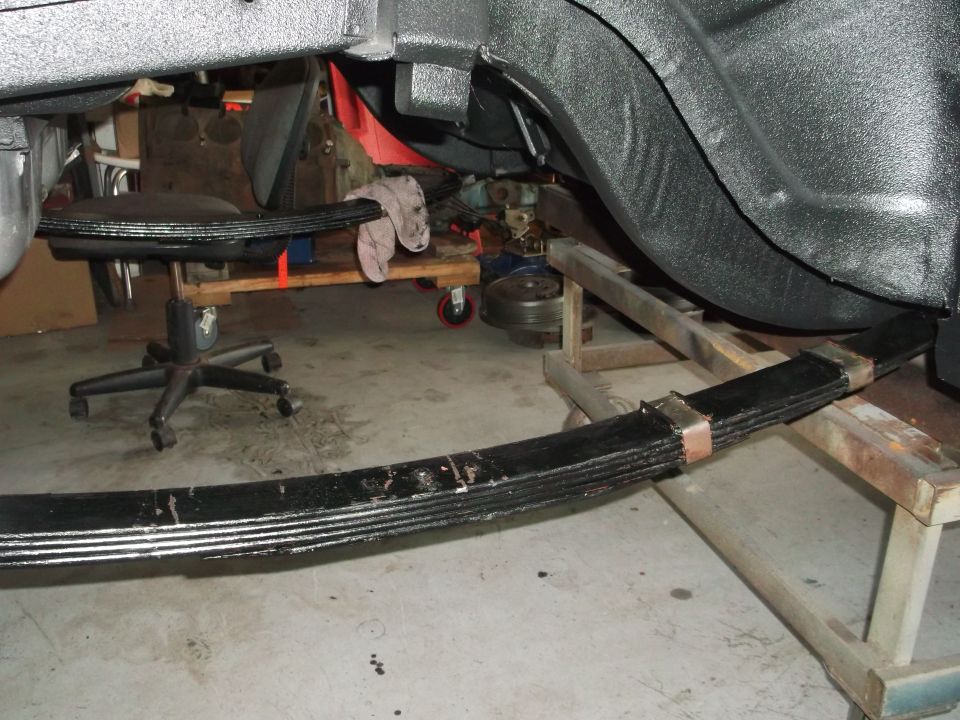 Black leaf springs on a stand beneath an undercoated rear wheel well in a restoration garage