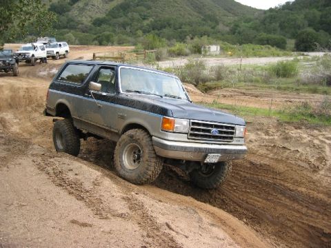 1989 Ford Bronco - Ford Bronco navigating a muddy trail with other vehicles present.