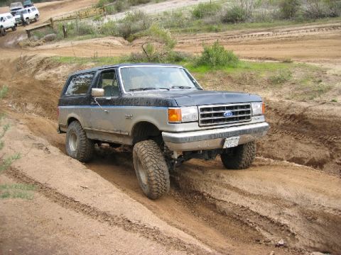 1989 Ford Bronco - This lifted Ford Bronco navigates a muddy off-road course with other vehicles visible in the distance.