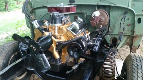 Engine bay of a green vehicle with a gold engine, black fan, and visible suspension components