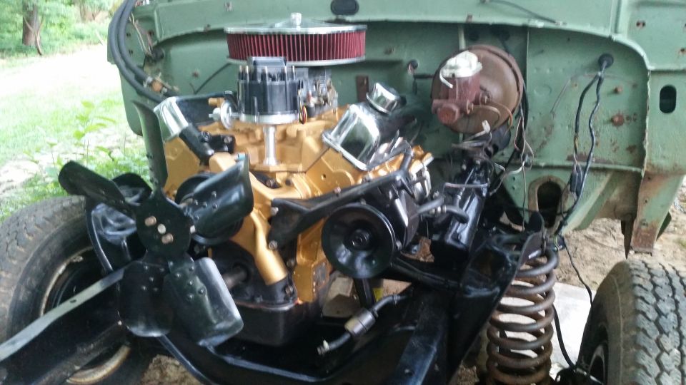 Engine bay of a green vehicle with a gold engine, black fan, and visible suspension components