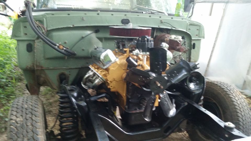 Front end of a green truck with engine exposed, showing V8 engine, air filter, and fan