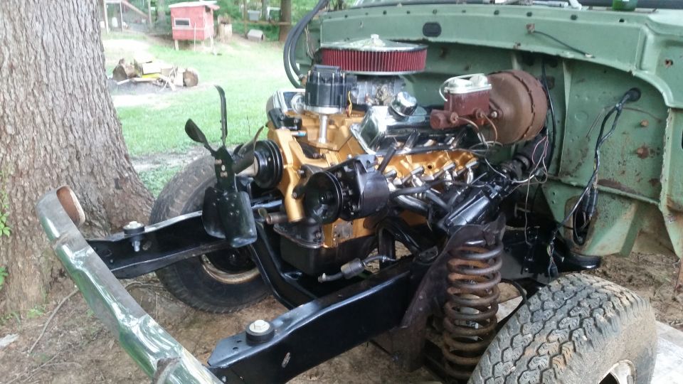 Engine and chassis of a green vehicle, with gold-colored engine components and black frame. Tires and suspension visible
