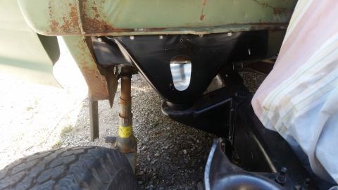 Close-up of vehicle frame with jack supporting it, showing suspension components and part of a tire