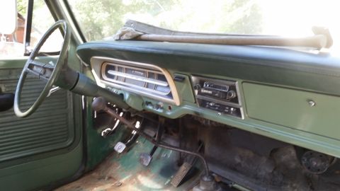 Green dashboard and steering wheel of an old truck with a radio and floor pedals