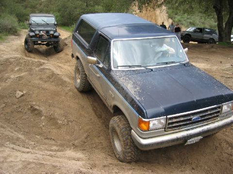 1989 Ford Bronco - A blue 1989 Ford Bronco navigates a dirt trail, with a Jeep following closely behind.