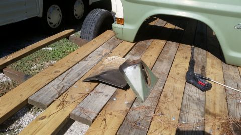 Green car fender section and other parts on wooden planks next to a trailer tire