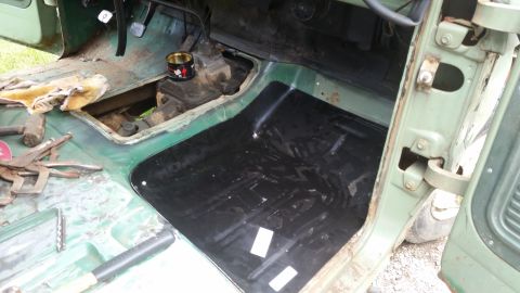 Vehicle interior showing removed floor pan, transmission tunnel, and tools. A new black floor mat is installed