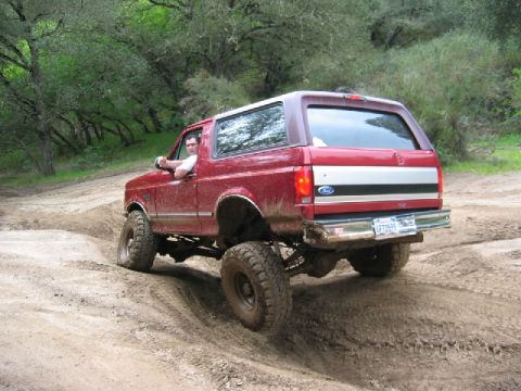 1989 Ford Bronco - Red 1989 Ford Bronco navigates a muddy off-road path.