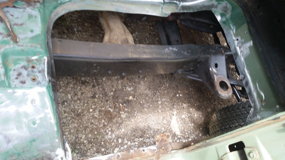 close-up of vehicle frame and suspension components, with gravel on the ground