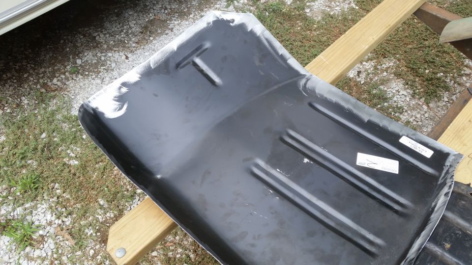Black metal car floor pan with reinforcing ribs, resting on wooden beams
