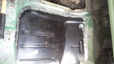 Vehicle floor pan with cutouts and exposed metal, a hammer visible on the left