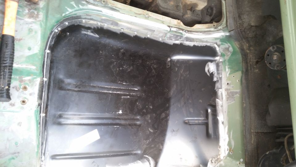 Vehicle floor pan with cutouts and exposed metal, a hammer visible on the left