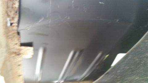 Close-up of a vehicle's undercarriage, showing some rust on the left and a dark panel with ribbed reinforcemen