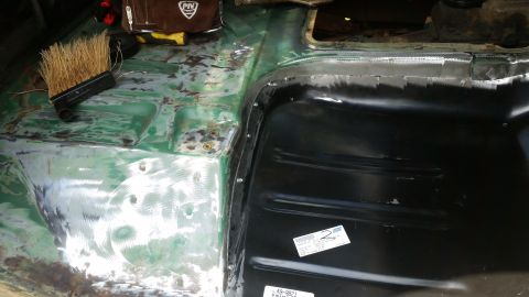 close-up of vehicle floor pan being repaired, showing green primer and new black metal panel
