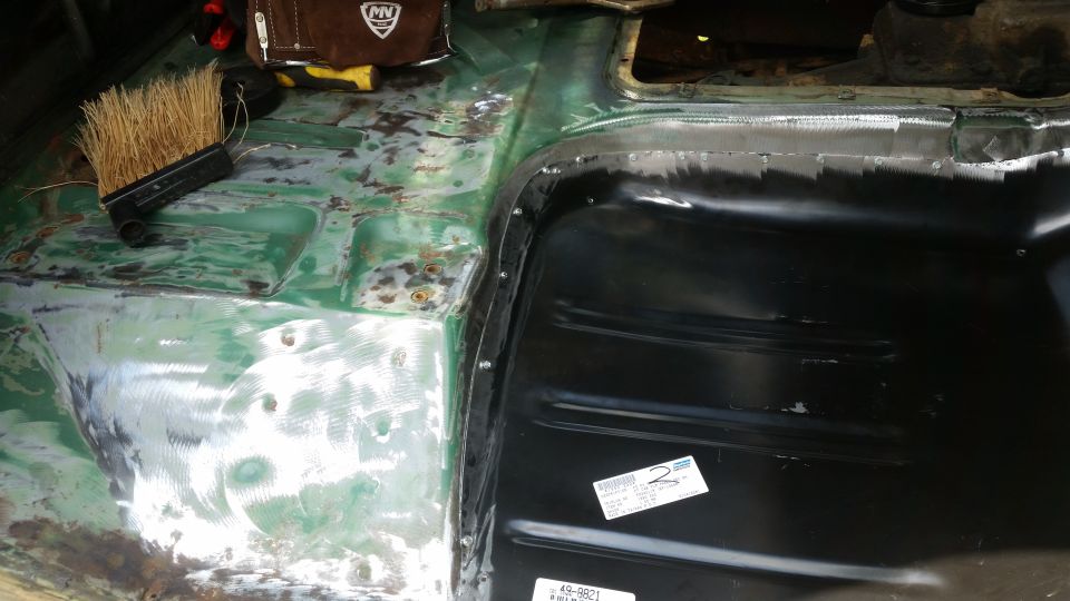 close-up of vehicle floor pan being repaired, showing green primer and new black metal panel