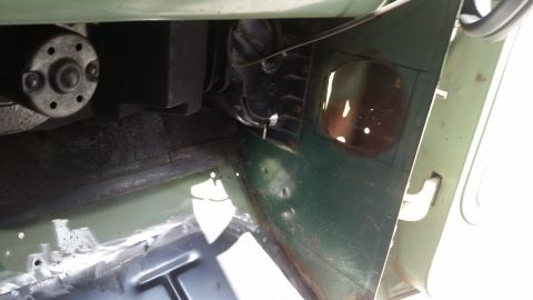 Interior view of green vehicle's engine bay and floor pan with visible metalwork