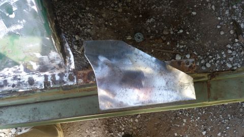 Metal patch welded onto a green vehicle's rusty door frame