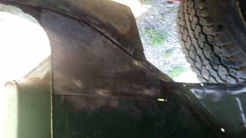 Close-up of a dark green vehicle body panel with a tire visible in the upper right