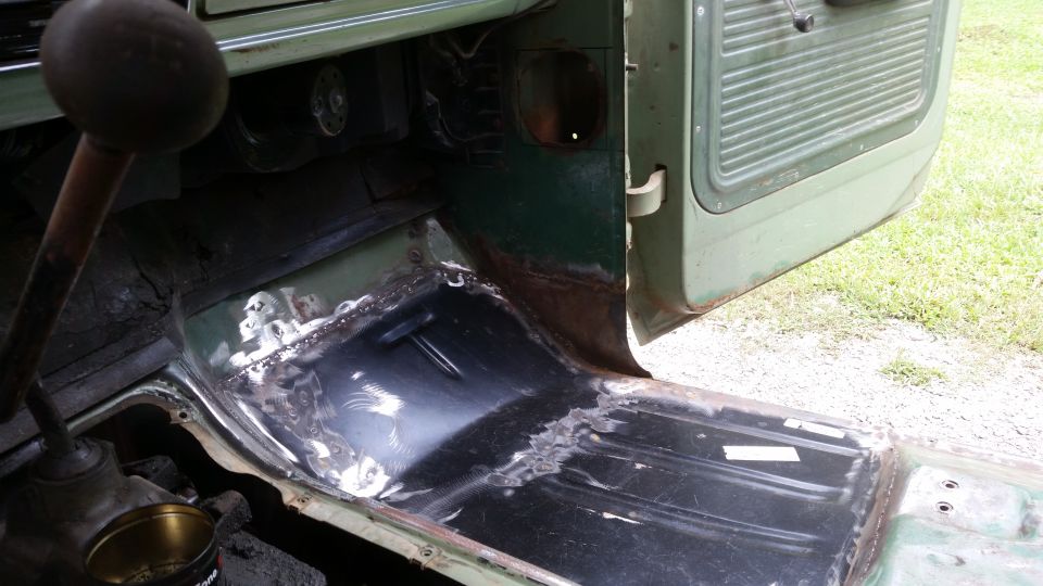Green vehicle interior floor with exposed metal and rust patches, showing a floor shifter and open door