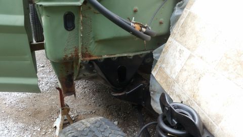 close-up of vehicle frame with rust and new black metal bracket welded in place, jack stands visible
