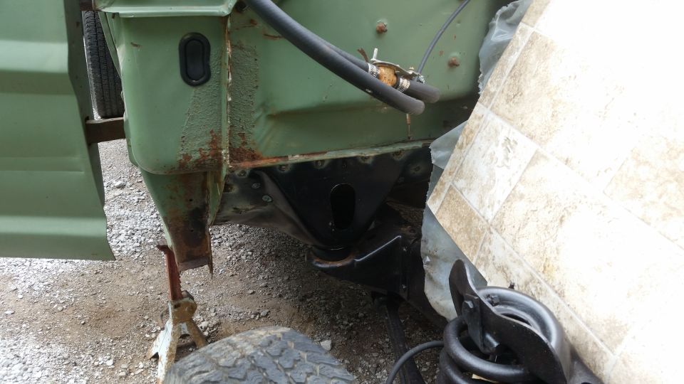 close-up of vehicle frame with rust and new black metal bracket welded in place, jack stands visible