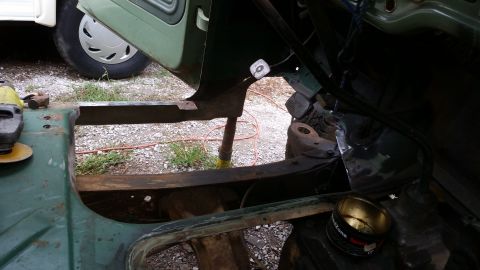 Green vehicle frame with grinding tool nearby; door open, showing interior structure. Part of another vehicle