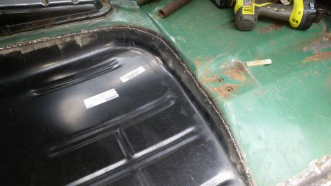 Interior floor pan and fuel tank with visible labels and a power tool in the background