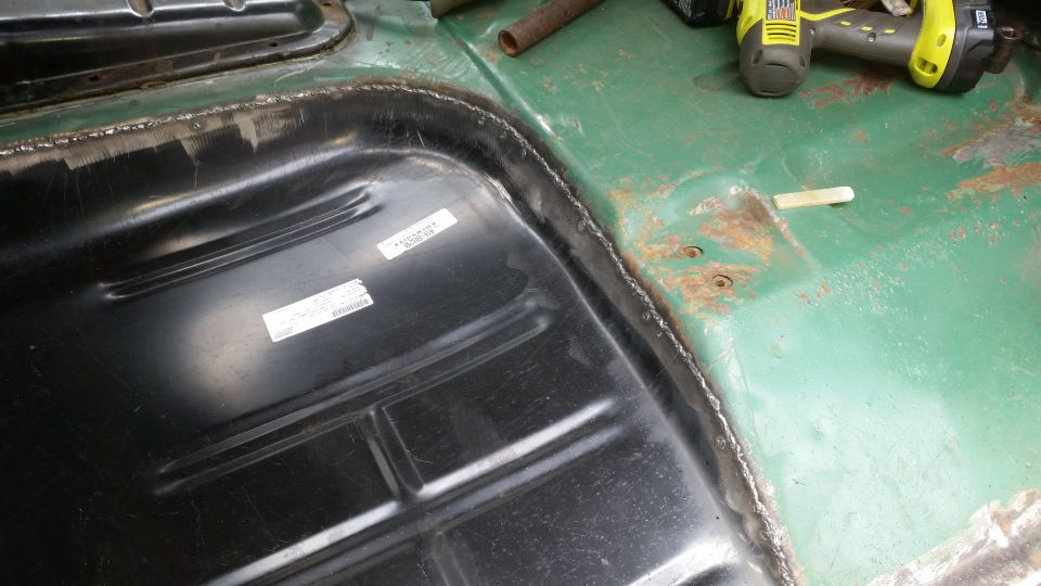 Interior floor pan and fuel tank with visible labels and a power tool in the background