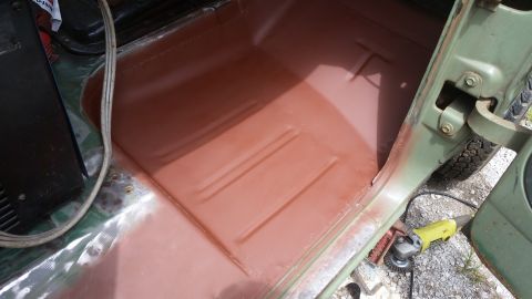 1978 Ford Bronco interior floor pan with red primer, showing door hinge and grinder