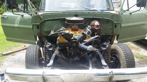 Green truck with hood removed, showing engine and front suspension