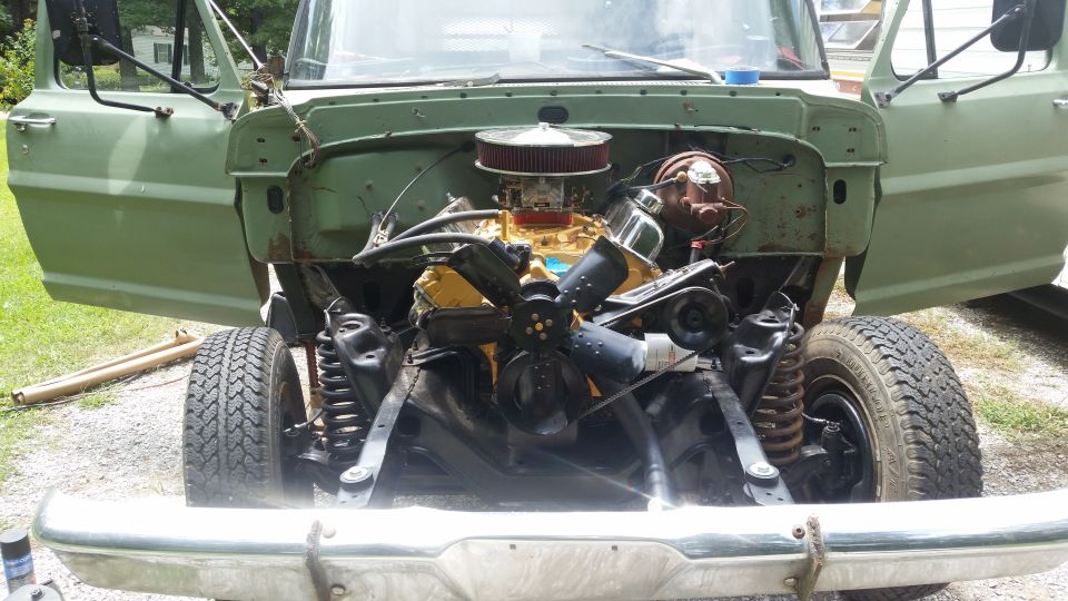 Green truck with hood removed, showing engine and front suspension
