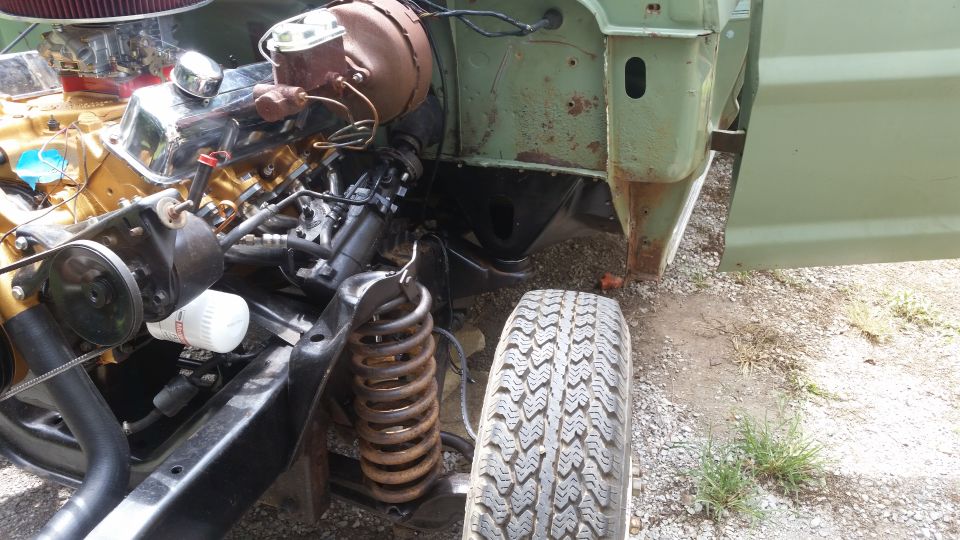 Green vehicle's engine bay and front suspension with a tire nearby