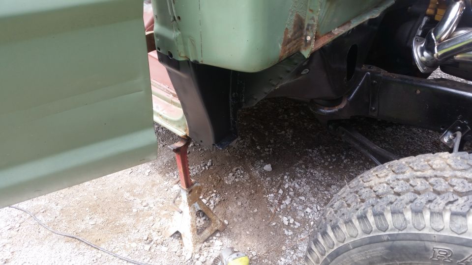 Close-up of vehicle frame and fender area undergoing repair, supported by an engine jack. Tire visible