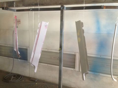 1964 Ford Fairlane - Car parts are suspended and being painted inside a booth, with spray paint marks on the wall.