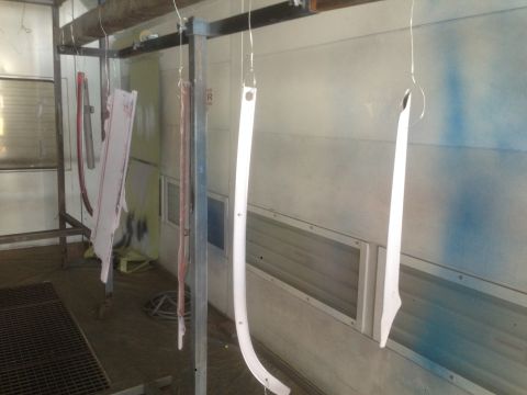 1964 Ford Fairlane - Automotive trim parts are suspended for painting inside a spray booth.