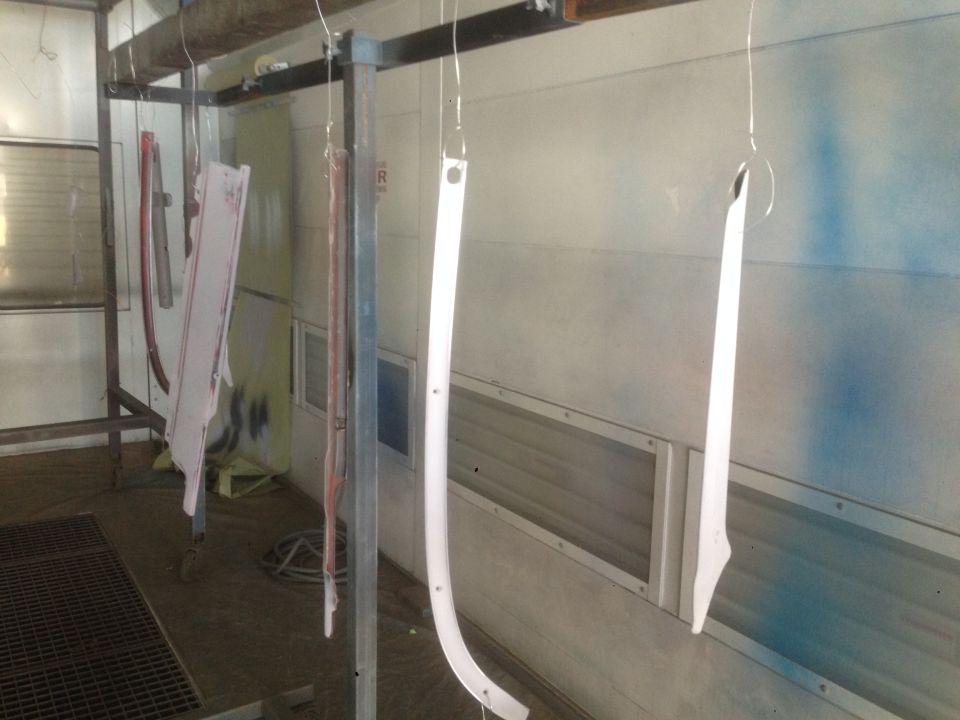 Car trim pieces hanging in a paint booth, some white, one red