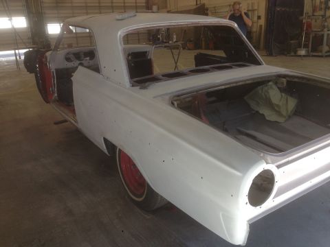 1964 Ford Fairlane - A white 1964 Ford Fairlane coupe in primer, showing its red wheels and open trunk, is in a workshop for restoration.