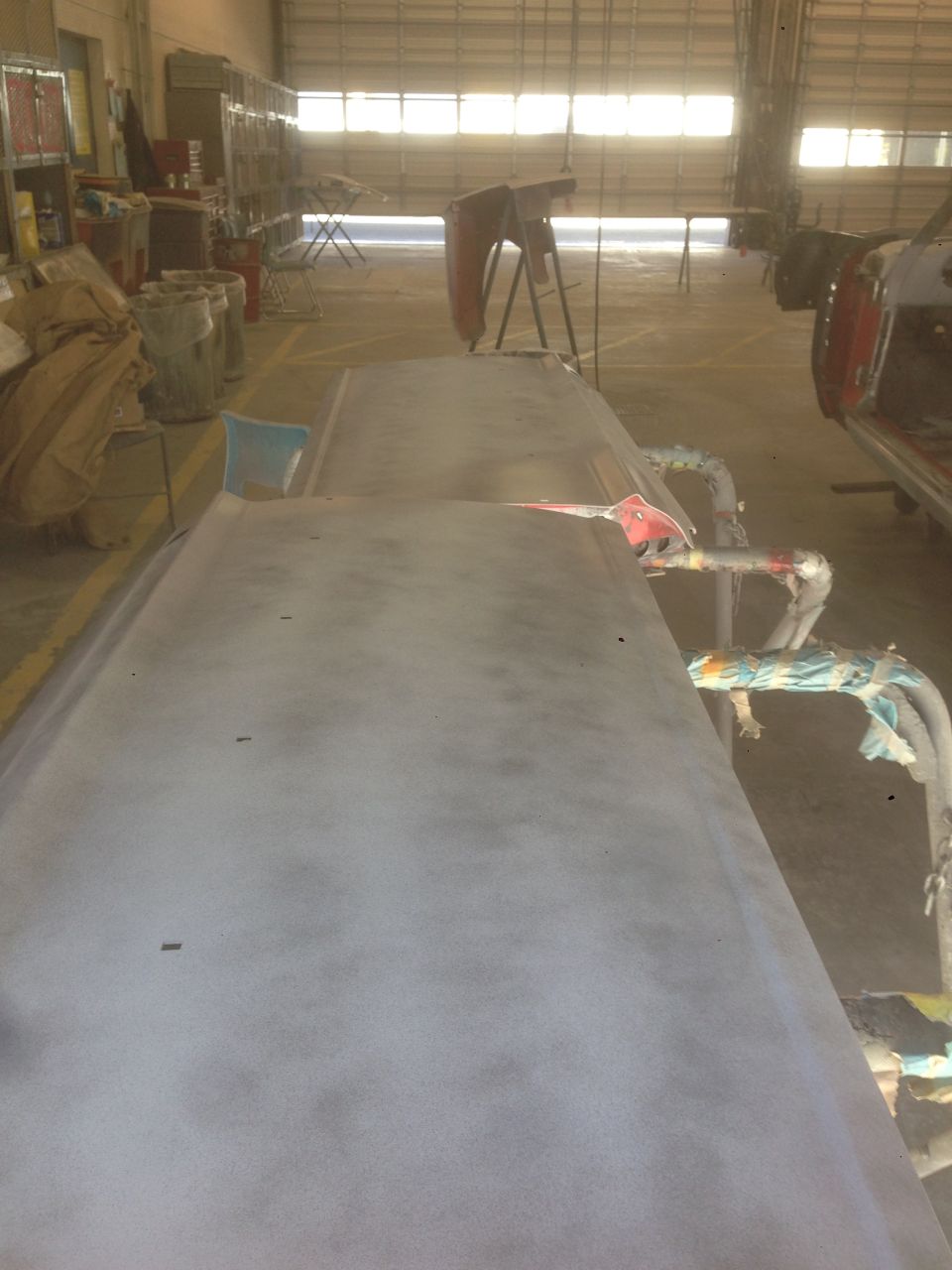 car hood covered in primer, in a workshop with another car body to the right