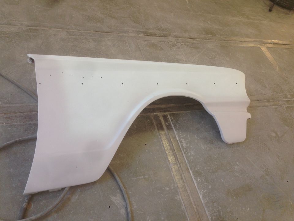 White car fender with primer, showing wheel arch and mounting holes