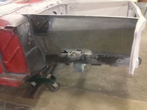 1964 Ford Fairlane - The chassis of a car is shown, with a red panel visible on the left side and the frame supported by jack stands.