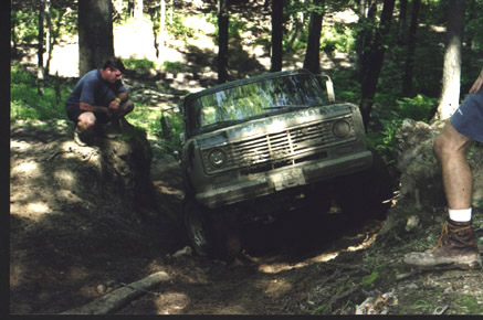 1991 Ford Bronco - An off-road vehicle attempts to traverse a challenging muddy terrain in a forest setting.