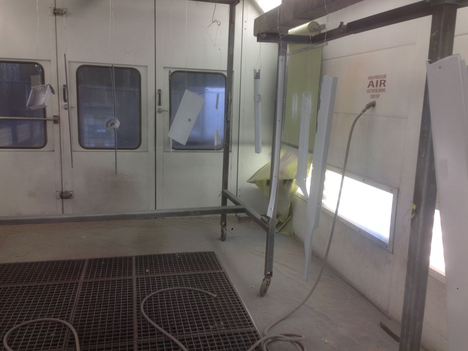 paint booth with parts hanging to be painted, including a metal panel and some trim pieces