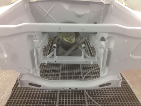 1964 Ford Fairlane - The engine bay of a vehicle, primed white and ready for further work, sits on a specialized grid floor.
