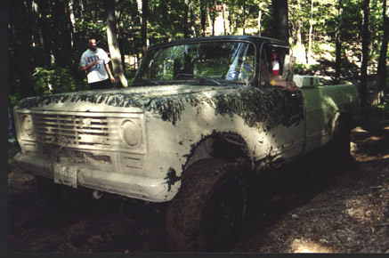 1991 Ford Bronco - A mud-splattered pickup truck is stuck in the dirt, surrounded by trees.