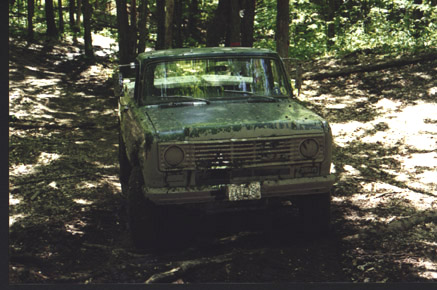 1991 Ford Bronco - A green pickup truck is parked on a dirt path in a wooded area.