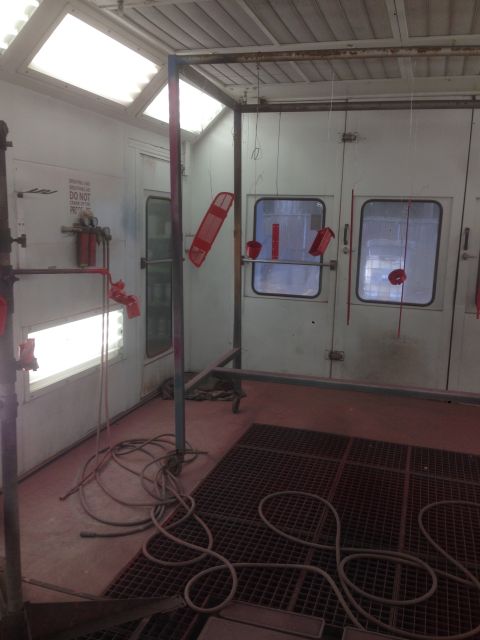 1964 Ford Fairlane - Red automotive parts are suspended for painting inside a spray booth, with hoses and equipment visible.